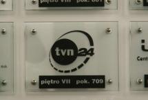 Logo TVN24 umieszczone na tablicy informacyjnej na parterze budynku.